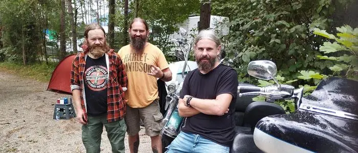 Drei Männer haben sich neben einem Motorrad aufgestellt und lächeln in die Kamera