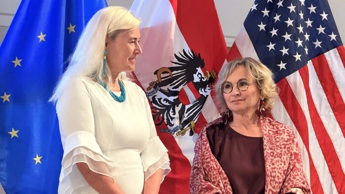 Österreichs Botschafterin Petra Schneebauer steht mit Bürgermeisterin Elisabeth Blanik (SPÖ) vor den Fahnen von Europa, Österreich und der USA