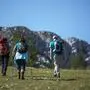 Drei wanderende Personen auf einer Alm, im Hintergrund sieht man eine felsige Bergkette