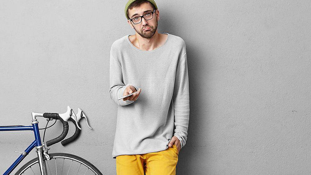 People, lifestyle and modern urban lifestyle concept. Picture of clueless young bearded European man holding gadget and shrugging shoulders, feeling confused while having problem with connection