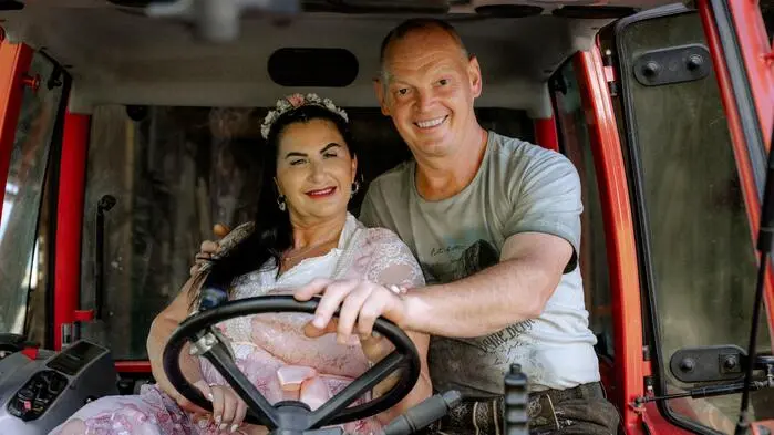 Ein Mann und eine Frau sitzen auf einem Traktor und lächeln in die Kamera.