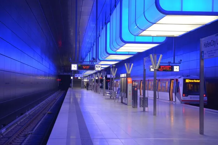 Die Hamburger Hochbahn wurde 1912 in Betrieb genommen und ist damit die zweitälteste U-Bahn Deutschlands. 100 Jahre nachdem die erste U-Bahn durch Hamburg fuhr, eröffnete der U-Bahnhof HafenCity Universität der neuen Linie U4. Der Blickfang: 12 riesige Leuchtcontainer, die von der Decke hängen. Jeder von ihnen wiegt 6 Tonnen und ist mit 280 LED ausgestattet, die den U-Bahnhof in ein zauberhaftes Licht eintauchen. Glatte dunkelbraune Metallplatten an der Wand und an der Decke reflektieren das Lichtschauspiel.