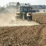 Ein Traktor zieht einen Pflug über ein Feld, dahinter erhebt sich eine Staubwolke 