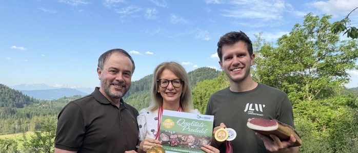 Drei Menschen halten Speck, Urkunden und Medaillen in die Kamera