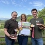 Drei Menschen halten Speck, Urkunden und Medaillen in die Kamera