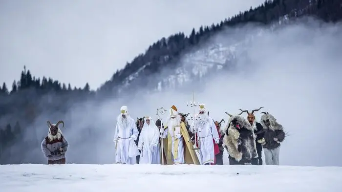 Der Apostel Thomas, der weiße Thomas, auch Lichtbringer genannt, die Nikolofrau, der Gabenbringer, auch Sackträger genannt, der Greis, die Thomashutzn sowie Krampusse unterwegs auf einer schneebedeckten Wiese