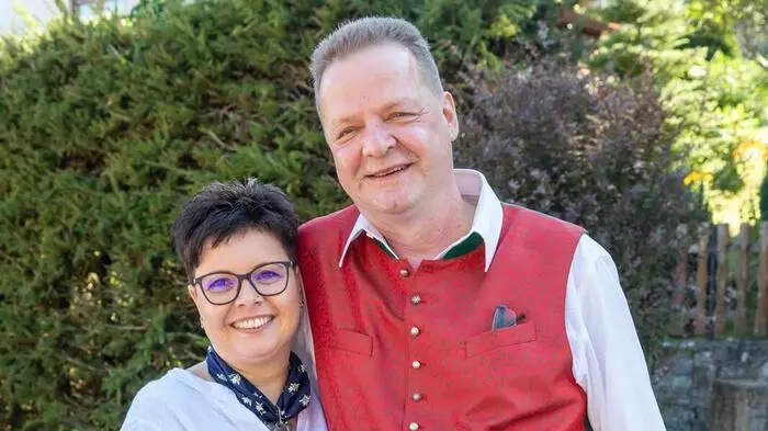 Ein Mann mit Trachtengilet und eine Frau mit kurzen Haaren und Brille lächeln in die Kamera
