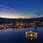 Drohnenaufnahme in der Dämmerung: See mit einem schwimmenden Adventkranz, dahinter eine weihnachtlich beleuchtete Stadt | Advent in Velden, Kärnten, Österreich