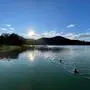 Ein See bei Sonnenuntergang, zwei Menschen schwimmen im Wasser.