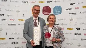 Eine Frau und ein Mann lächeln in die Kamera. In den Händen halten sie Auszeichnungen.