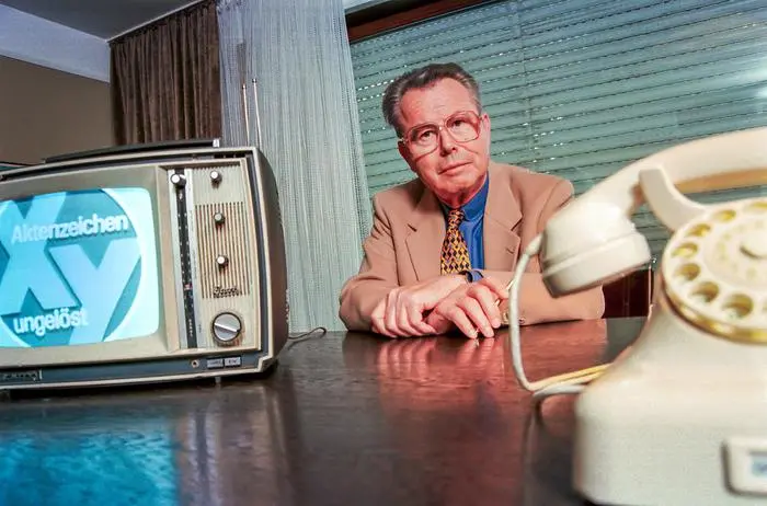 Eduard Zimmermann, Fernsehmoderator von Aktenzeichen X... ungelöst, Unterföhring, September 1997 Deutschland, Unterföhring, 23.09.1997, Eduard Zimmermann, 1929-2009, Fernsehmoderator von Aktenzeichen X... ungelöst, in seinem Büro, mit altem Telefon Siemens W 48 und Fernseher von Graetz, beide aus der Zeit um 1967, als die Sendung im ZDF startete, über Video wird Fernsehbild Aktenzeichen von 1967 eingespielt, von 1967 bis Oktober 1997 moderierte Zimmermann 300 XY-Folgen, Kriminalität, Verbrechen, Verbrechensbekämpfung, Schreibtisch, Fernsehgeschichte, TV-Geschichte, TV-Fahndung, Fahndung im Fernsehen, dunkel, 1990er Jahre, Geschichte, historisch, *** Eduard Zimmermann, television presenter of Aktenzeichen X ungelöst, Unterföhring,