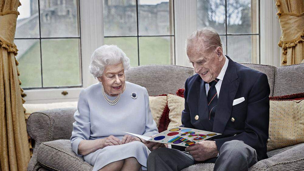 Königin Elizabeth II. und ihr Mann Prinz Philip betrachten lächelnd eine farbenfrohe Karte.