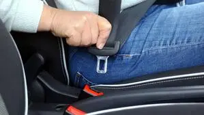 Eine rechte Hand hält eine Gurtschnalle und führt sie zum Verschluss an einem Autositz