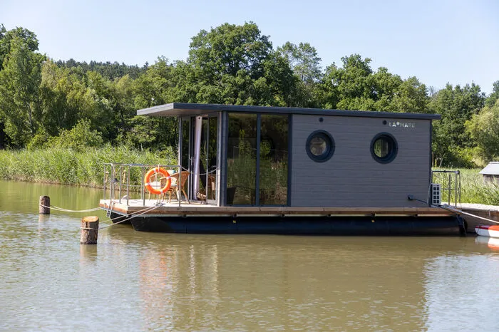 Wie ein grauer Mini-Bungalow, umgeben von Schilf, thront das Boot auf dem Wasser und bietet Wohnküche, Schlafkoje, Badezimmer und WC.