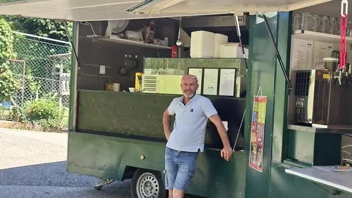 Ein Mann lehnt an einem geöffneten grünen Imbisswagen, daneben steht noch ein Wagen