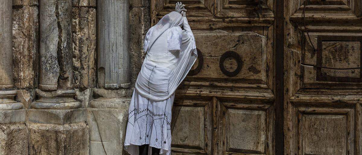 Eine Frau betet in der Karwoche vor dem verschlossenen Tor der Grabeskirche in Jerusalem