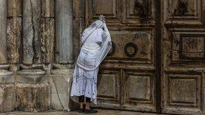 Eine Frau betet in der Karwoche vor dem verschlossenen Tor der Grabeskirche in Jerusalem