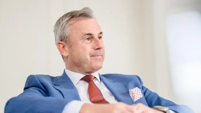 Norbert Hofer sitzt in einem blauen Anzug mit weißem Hemd und einer roten Krawatte bei einem Gespräch.