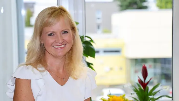 Eine blonde Frau in weißer Bluse lächelt in die Kamera