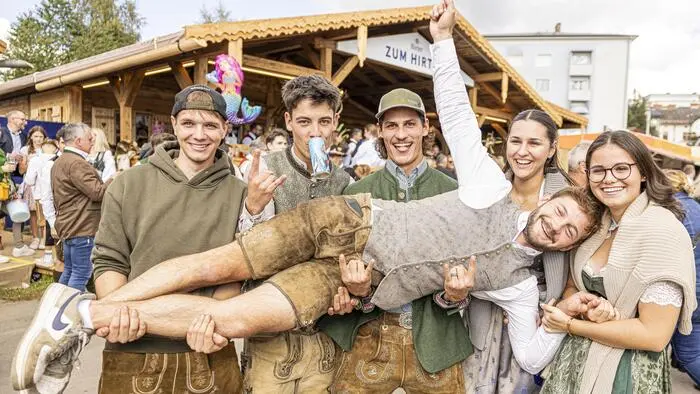 Vier junge Männer und zwei junge Frauen in Tracht posieren für ein Foto. Sie tragen einen der Männer auf Händen.