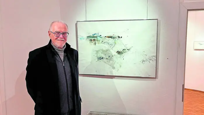 Ein Mann steht vor einem Kunstwerk und lächelt in die Kamera.