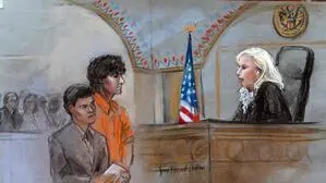 Gerichtszeichnung zeigt den Boston-Marathon Attentäter Dzhokhar Tsarnaev stehend in einem orangen Overall vor dem Pult der Richterin. Neben ihm steht ein etwas kleinerer Mann