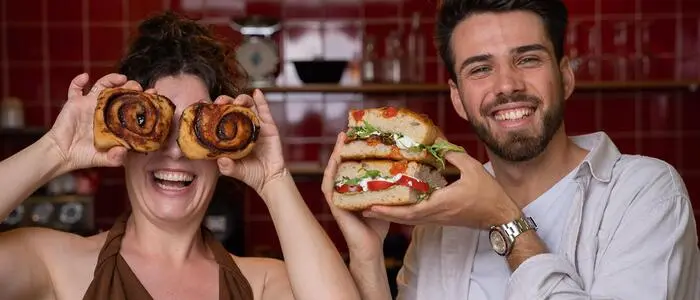 Die beiden gut gelaunten jungen Gastronomen in ihrem Lokal mit roten Fliesen im Hintergrund, sie hält Zimtschnecken vor ihre Augen, er präsentiert eine Focaccia