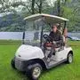 Ein Mann in Arbeitsbekleidung sitzt in einem Golfmobil auf einer Wiese vor einem See