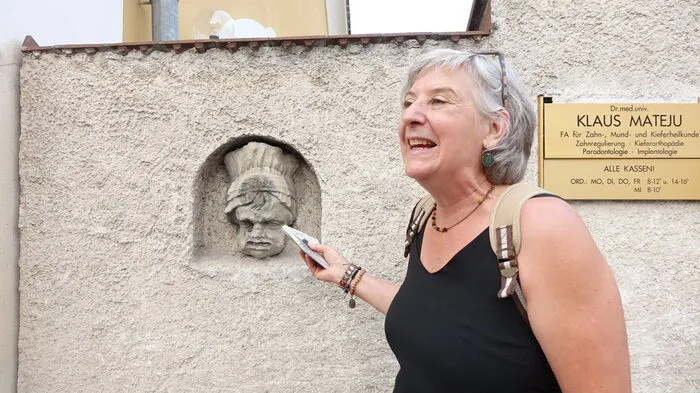 Ingeborg Hofbauer am Start ihres Literaturspazierganges durch Birkfeld an der Mauer des Schlosses Birkenstein. Man beachte dabei die Zahnmode der Skulptur und das Namensschild rechts von Hofbauer.