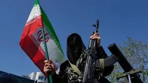Eine voll verhüllte iranische Frau hält in der rechten Hand eine iranische Flagge und in der linken eine Waffe