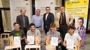 Mehrere junge Männer hocken hinter ihren selbst gefertigten Tischlerarbeiten, dahinter stehen mehrere Männer