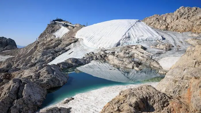 Der Eispalast wird durch eine Polyesterplane geschützt, an seinem Fuß hat sich ein Schmelzwassersee gebildet