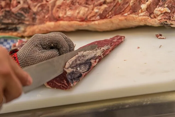 Mit einem scharfen Messer wird die dunkle Kruste abgeschnitten und danach offenbart sich die intensiv dunkelrote Farbe des gereiften Fleisches