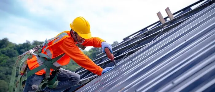 Ein Arbeiter kniet für Montagearbeiten auf einem Hausdach