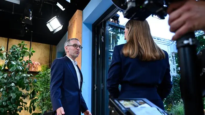  FPÖ-Bundesparteiobmann Herbert Kickl und Moderatorin Simone Stribl stehen in einer Tür. Auf sie ist eine Kamera gerichtet.