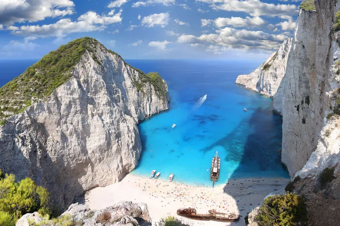 Navagio Bucht - Griechenland. Die “Schmugglerbucht” auf Zakynthos ziert viele Reisekataloge. Kein Wunder: Umgeben von Klippen kann man hier auf die weiß-blaue Bucht mit ihrem Schiffswrack blicken. 1980 erlitt ein mit geschmuggelten Zigaretten beladenes Schiff vor der Küste Schiffbruch, dieses wurde über die Jahre am Strand angespült. Wer sich die Aussicht nicht von hunderten Touristen trüben lassen will, sollte sich schon früh morgens oder am späten Nachmittag auf den Weg zur Bucht machen.