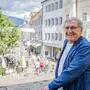 Ein Mann mit Brille und grauen Haaren trägt ein blaues Sakko und lächelt in die Kamera. Im Hintergrund eine Stadt