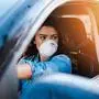 Young woman driving car with protective mask on her face.  Healthcare, virus protection, allergy protection concept.