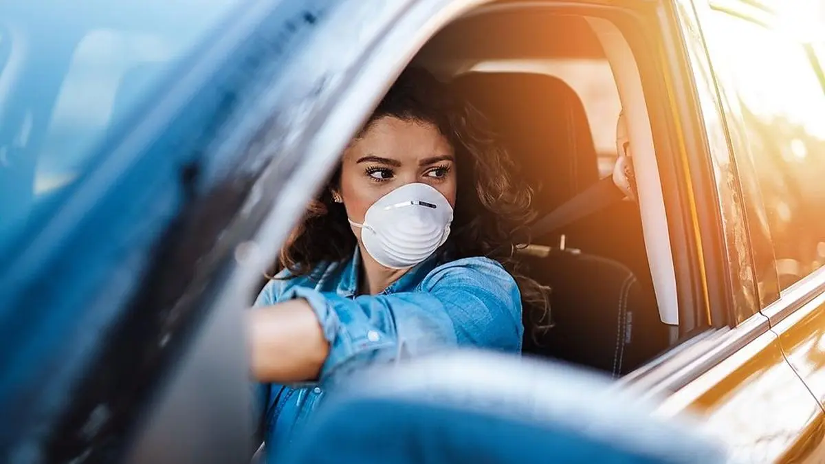 Young woman driving car with protective mask on her face.  Healthcare, virus protection, allergy protection concept.