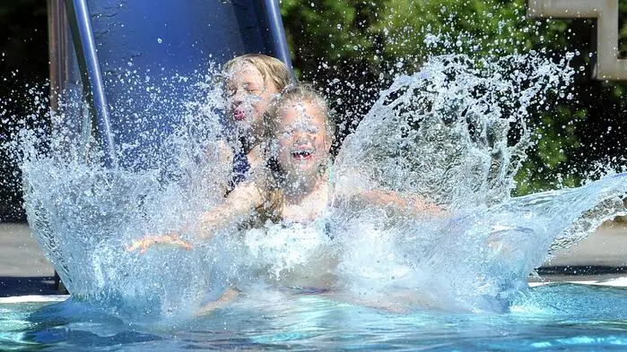 Das Bild zeigt zwei Kinder, die über eine Wasserrutsche in einen Pool rutschen