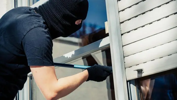 Ein mit Sturmhaube bekleideter Mann versucht, mit einem Brecheisen ein Hausfenster aufzubrechen