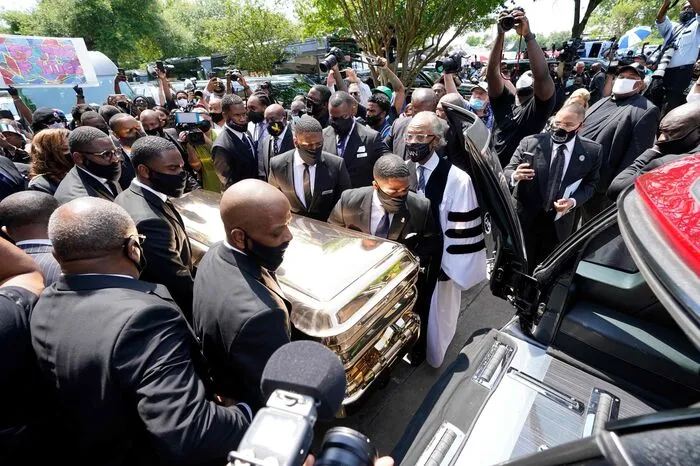 Unter dem wachsamen Blick Reverend Sharptonswird George Floyds Sarg in einen Leichenwagen geladen. Als die Leiche aus der Kirche "The Fountain of Praise" in Houston gebracht wurde, reckten viele Besucher ihre Faust als Zeichen des Kampfes gegen Rassismus in die Höhe.
