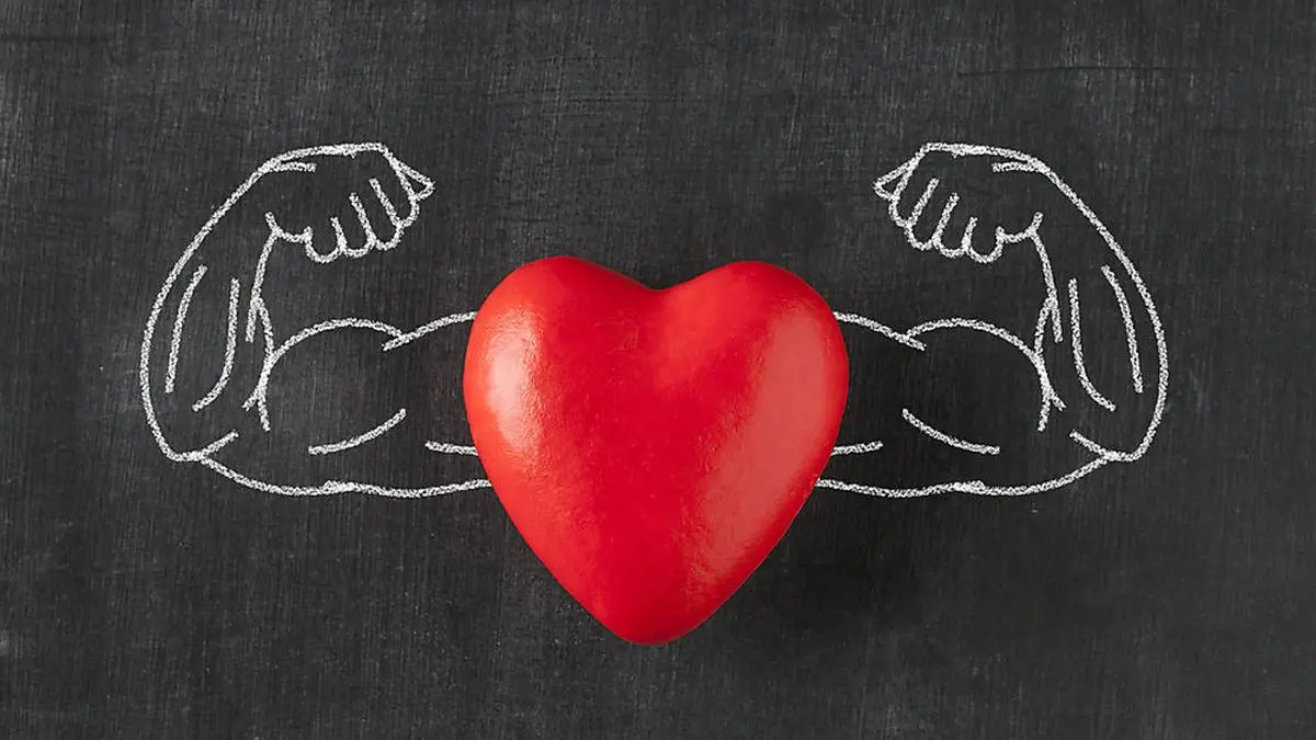 Heart with muscular arms drawn on blackboard