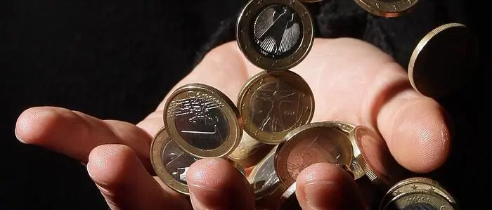 Euromünzen rieseln in eine ausgestreckte Hand