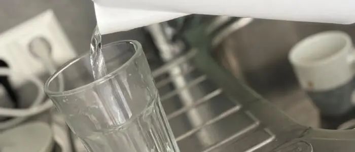 Nahaufnahme von einem Wasserkocher, der ein Glas mit Wasser füllt