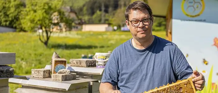 Ein Mann hält einen Stock voller Bienen in den Händen und blickt in die Kamera