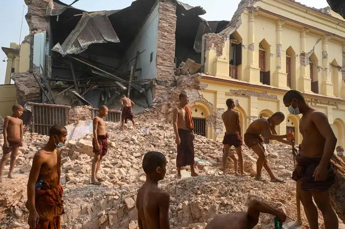 TOPSHOT - Buddhist monks stand on rubble as they clear up debris at the damaged Thahtay Kyaung Monastery in Mandalay on April 1, 2025, four days after a major earthquake struck central Myanmar. Four days after the shallow 7.7-magnitude earthquake that killed more than 2,000 people, many people in Myanmar are still sleeping outdoors, either unable to return to ruined homes or afraid of further aftershocks. (Photo by Sai Aung MAIN / AFP)