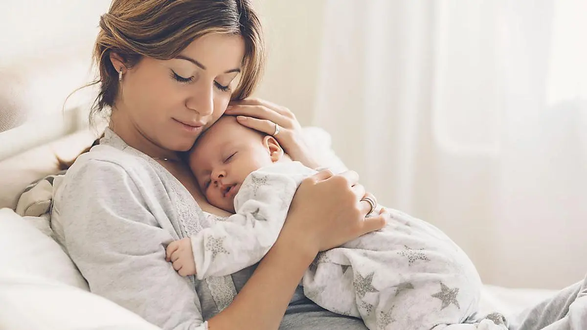 Loving mom carying of her newborn baby at home. Bright portrait of happy mum holding sleeping infant child on hands. Mother hugging her little 2 months old son.
