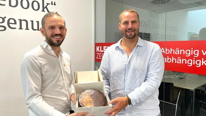 Zu sehen sind zwei Männer im weißen Hemd, die eine Torte halten