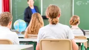Ein Lehrer steht in einer Schulklasse vor einer Tafel, vor ihm sitzen Schüler